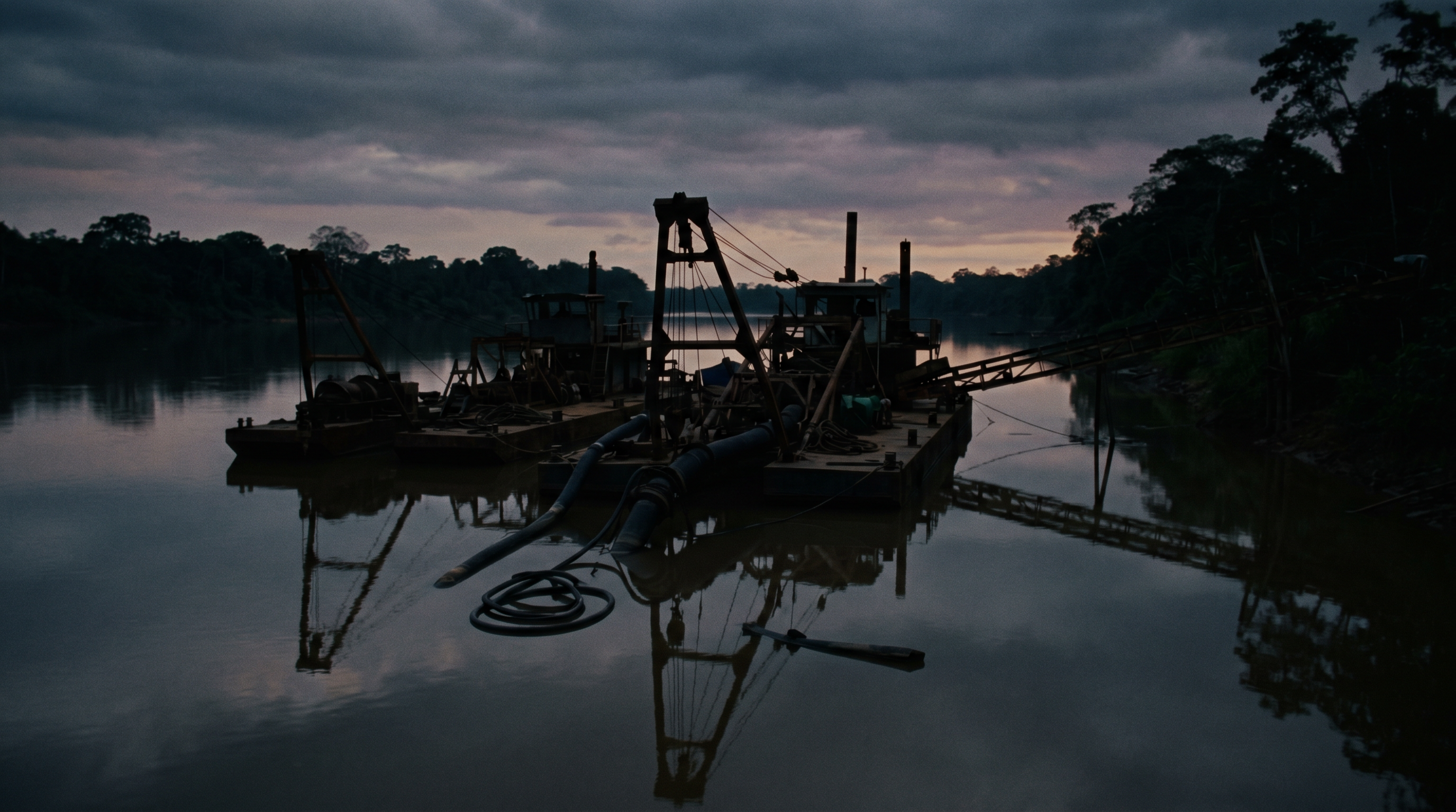 Silhouettes of dredging barges on a tropical river at dusk.